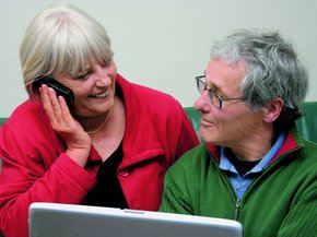 Пожилая пара у ноутбука: смотрят друг на друга, женщина говорит по телефону
